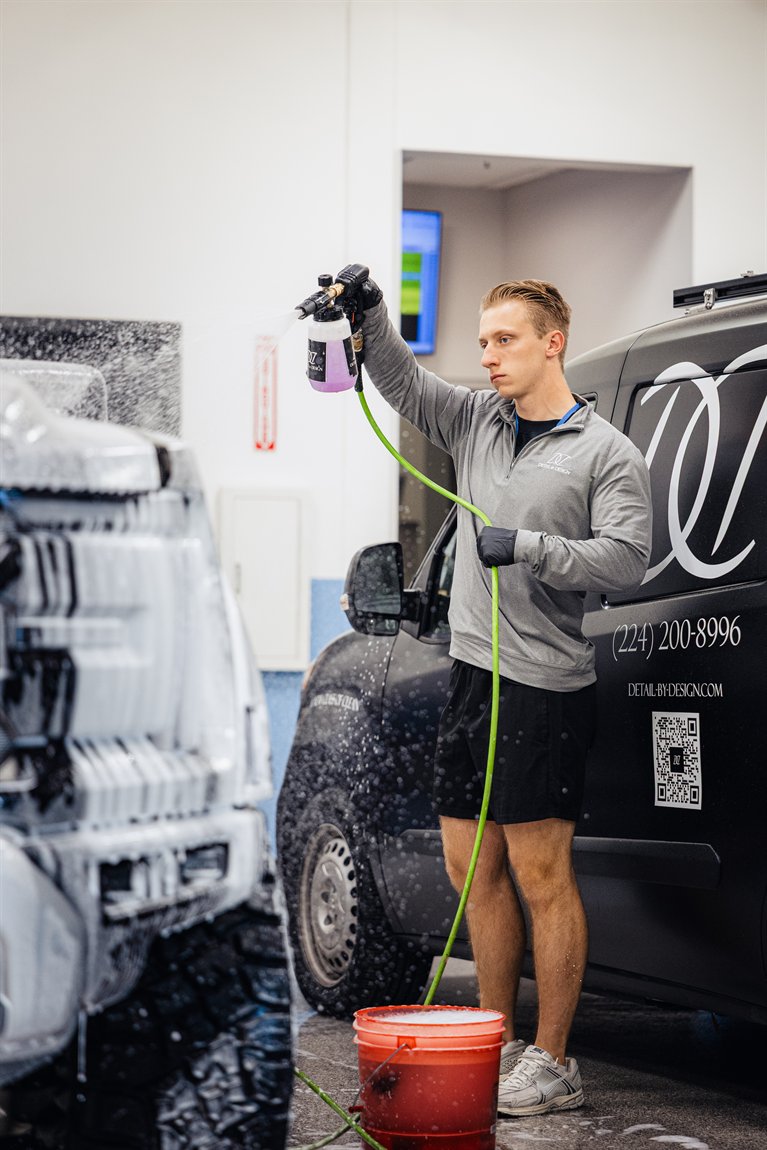 A Detail By Design founder foaming a vehicle beside the branded mobile studio van.