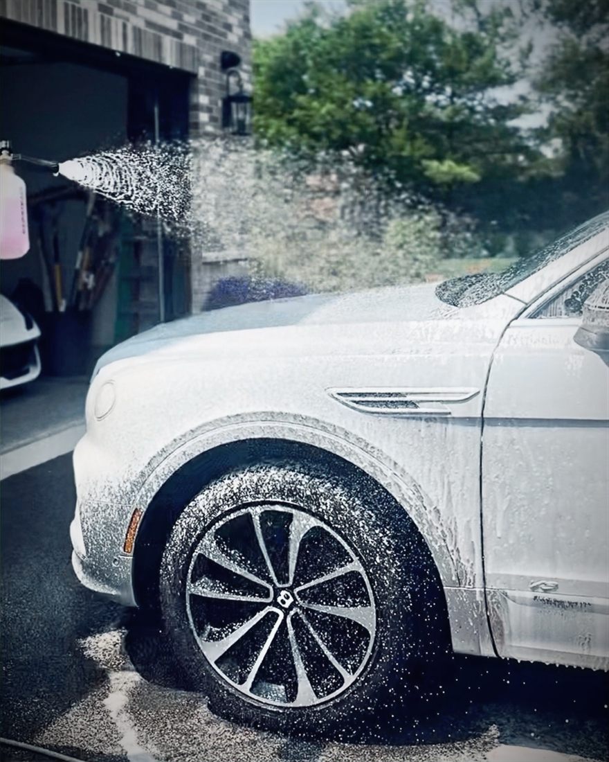 A white Bentley Bentayga covered in snow foam during a hand wash.